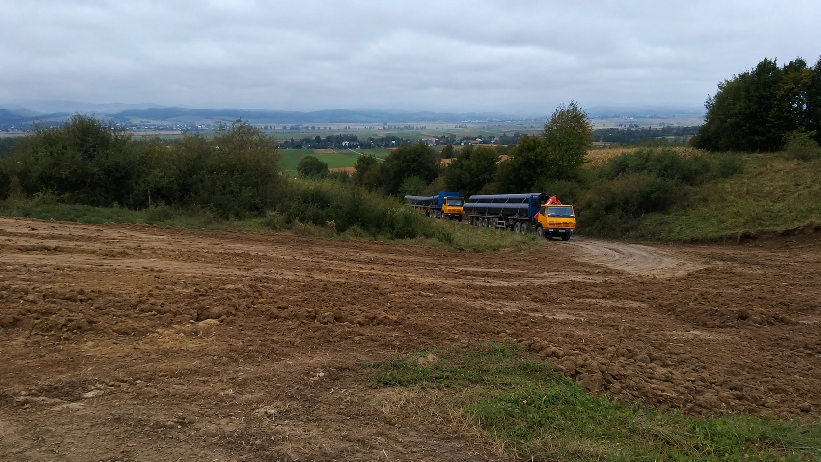 Ciężarówki wiozące rury o dużych średnicach na plac budowy.